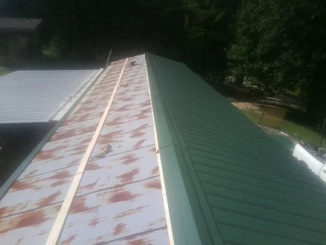 Old rusted panels beside newly installed green metal roofing — Wind Damage Roof Repair by Roofing Brothers in Belle Chasse