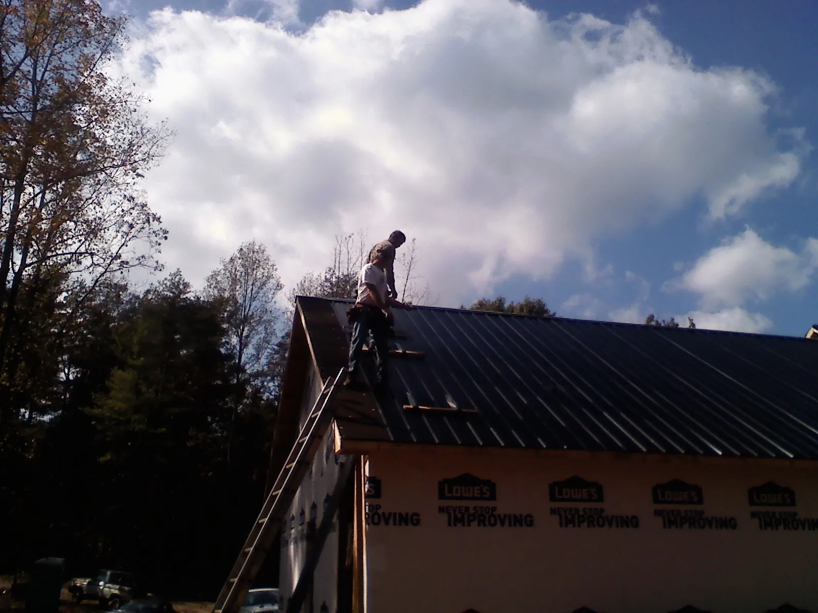 Roofer fastening dark metal panels high against a cloudy sky, from a Roof Inspection job in Belle Chasse