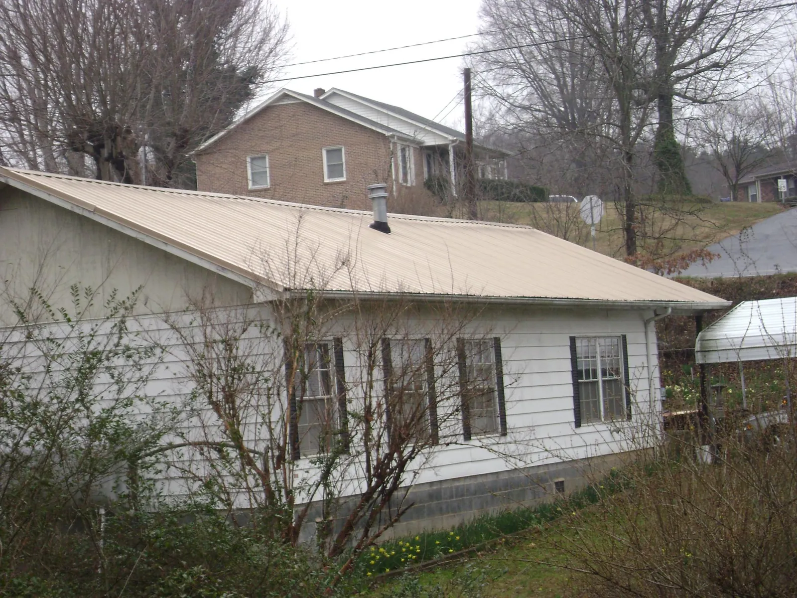 Tan metal roof on a white sided house set into a hillside — Commercial Roofing by Roofing Brothers in Belle Chasse