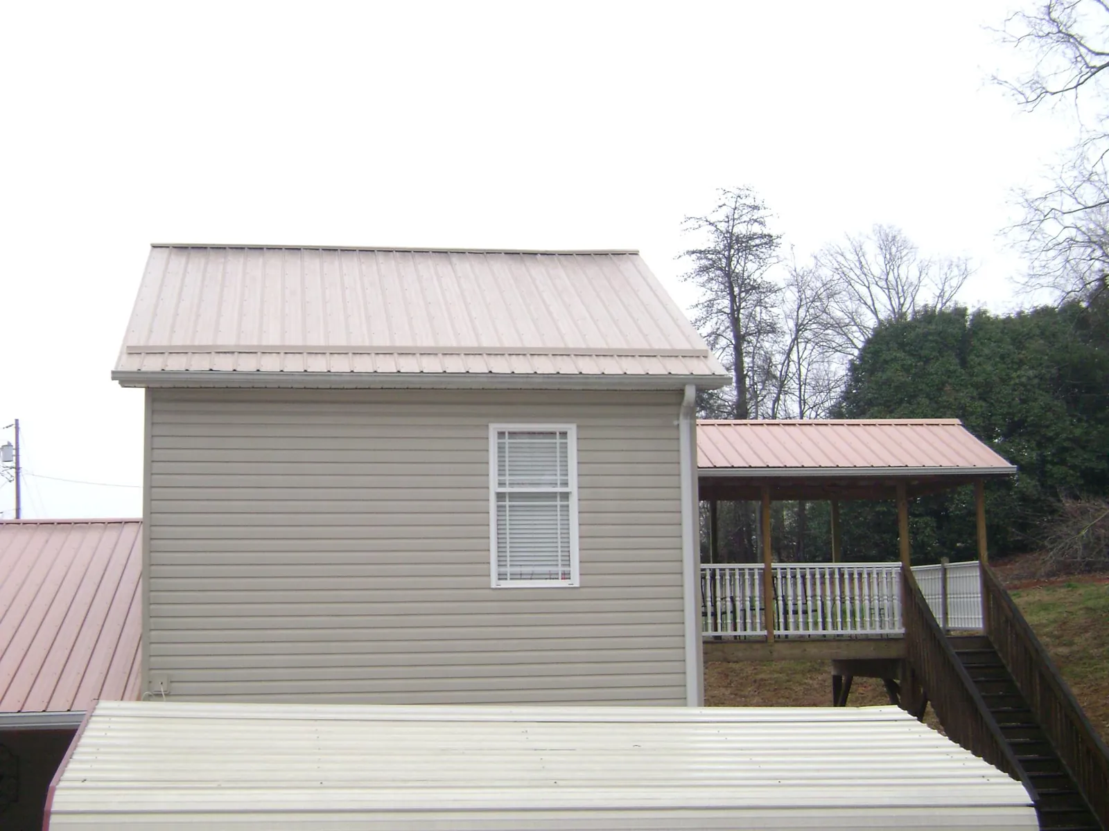 Tan metal roofs on a two story addition and attached porch, from a Roof Replacement job in Belle Chasse